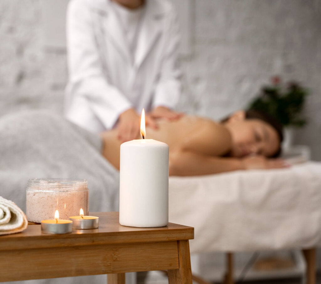 Une femme recevant un massage du dos dans un spa, avec des bougies allumées et des produits de soin au premier plan.