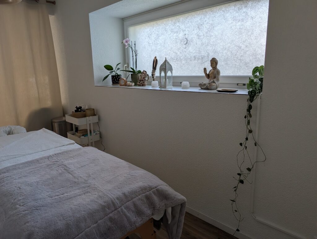 Espace Sélènes, table de massage à côté d'une fenêtre dans un espace paisible et cosy.