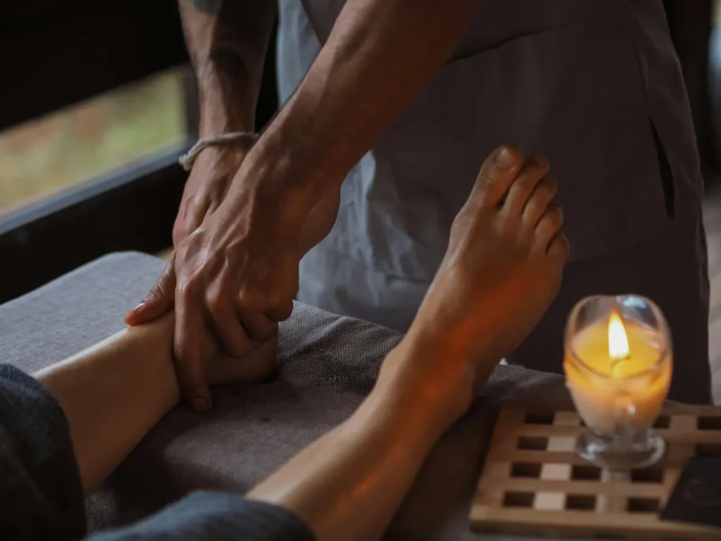 Illustration_reflexologie_equilibre_global | Espace Sélènes Une personne recevant un massage des pieds par un professionnel dans une ambiance apaisante avec une bougie.